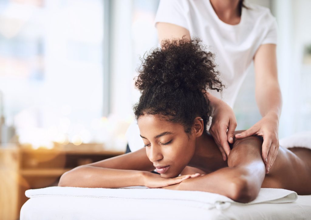 Massage therapist massaging young woman’s shoulder during touch therapy session