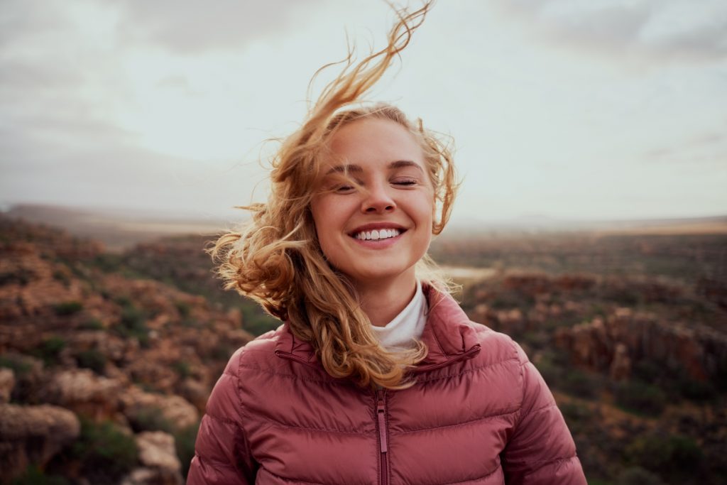 Smiling young woman overcomes depression through touch therapy with mountain background

